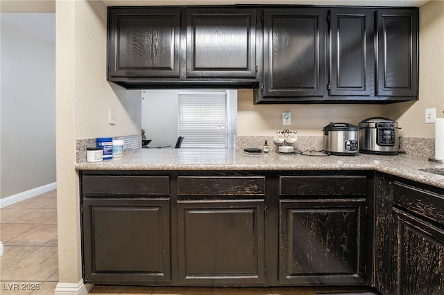 kitchen featuring light tile patterned floors, baseboards, dark cabinets, and light countertops