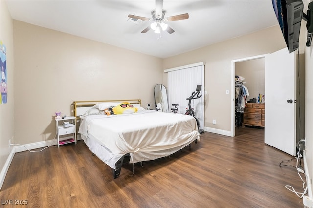 bedroom with a walk in closet, baseboards, wood finished floors, and a ceiling fan