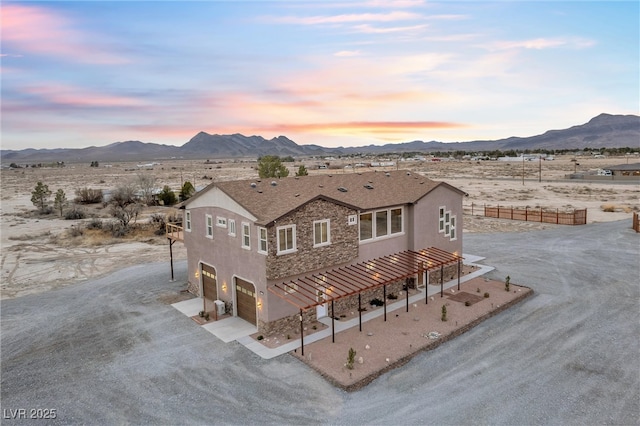 back of house at dusk featuring a mountain view, stone siding, and stucco siding