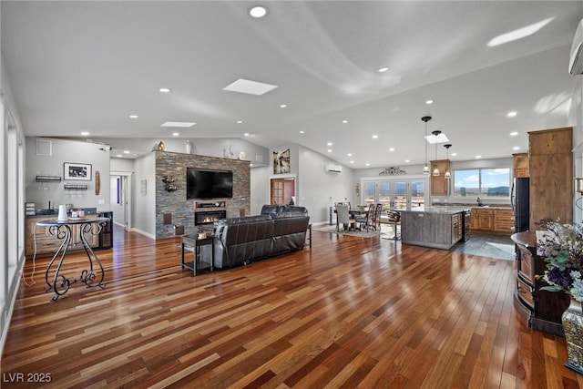 living room with a stone fireplace, vaulted ceiling, a wall unit AC, and wood finished floors