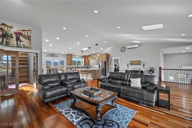 living room featuring visible vents, a wall unit AC, hardwood / wood-style floors, recessed lighting, and vaulted ceiling with skylight