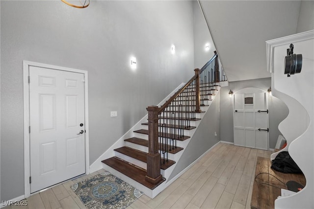 stairway featuring baseboards, wood finished floors, and a towering ceiling