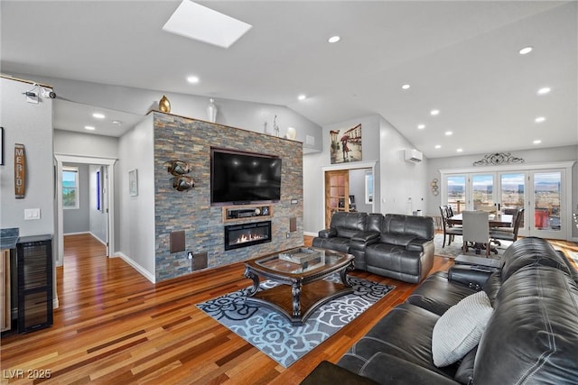 living room featuring vaulted ceiling, a fireplace, light wood finished floors, and a wall mounted AC