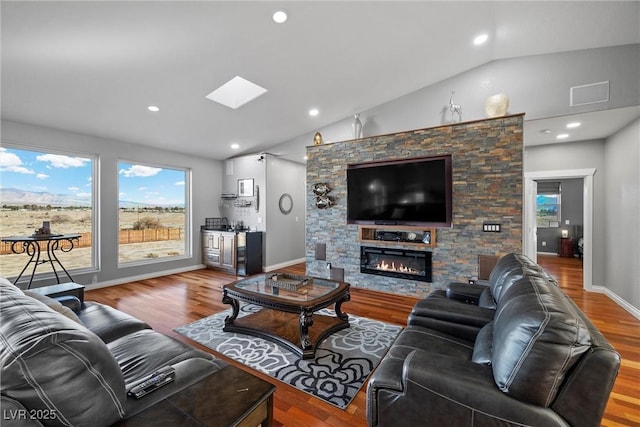 living area featuring a glass covered fireplace, wood finished floors, recessed lighting, vaulted ceiling with skylight, and baseboards