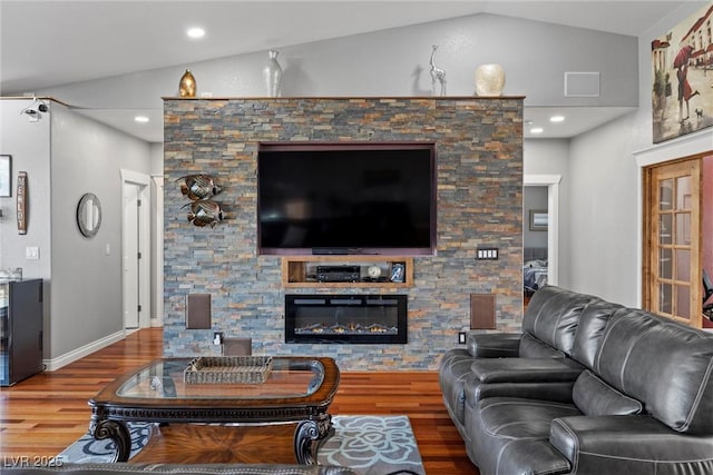 living area with a stone fireplace, wood finished floors, baseboards, and vaulted ceiling