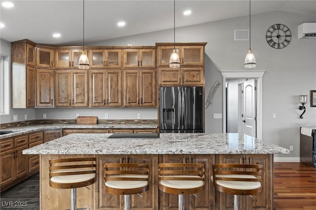 kitchen featuring brown cabinets, a kitchen island, a wall unit AC, stainless steel fridge, and vaulted ceiling