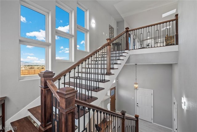 stairway with baseboards, a towering ceiling, and wood finished floors