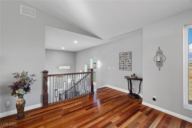 hall with wood finished floors, visible vents, baseboards, lofted ceiling, and an upstairs landing