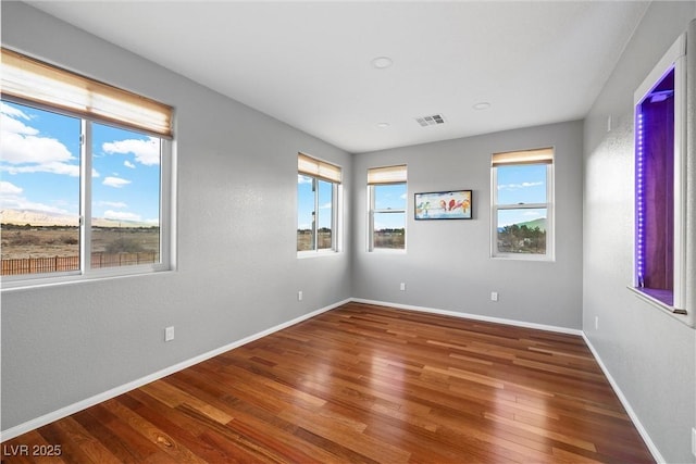 empty room featuring a wealth of natural light, visible vents, baseboards, and hardwood / wood-style flooring