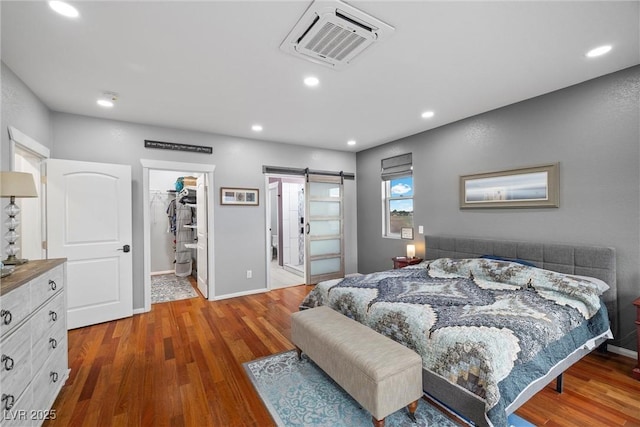 bedroom featuring a barn door, a spacious closet, wood finished floors, and visible vents