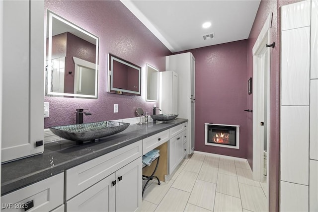 full bath with visible vents, a textured wall, and a sink