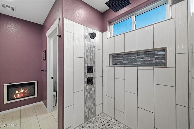 bathroom featuring visible vents, tiled shower, a glass covered fireplace, toilet, and a textured wall