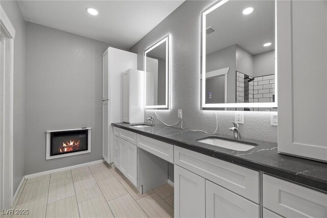 full bath featuring a glass covered fireplace, double vanity, visible vents, and a sink