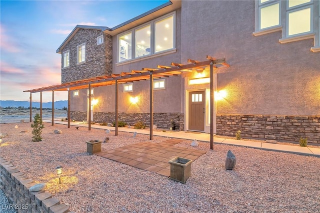 exterior space featuring stone siding, stucco siding, a pergola, and a patio