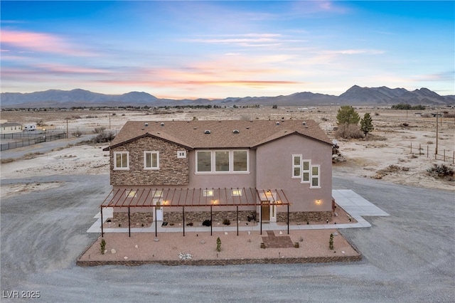 view of front facade featuring fence, a mountain view, stone siding, and stucco siding