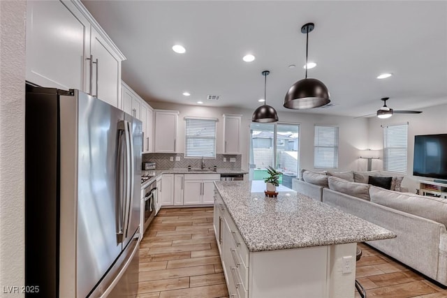 kitchen featuring wood tiled floor, open floor plan, backsplash, and stainless steel appliances