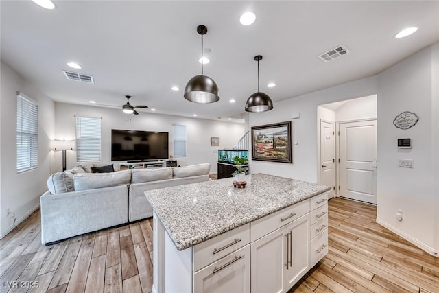 kitchen featuring visible vents, a kitchen island, light wood-style flooring, and a ceiling fan