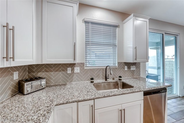 kitchen featuring backsplash, light stone countertops, dishwasher, white cabinets, and a sink