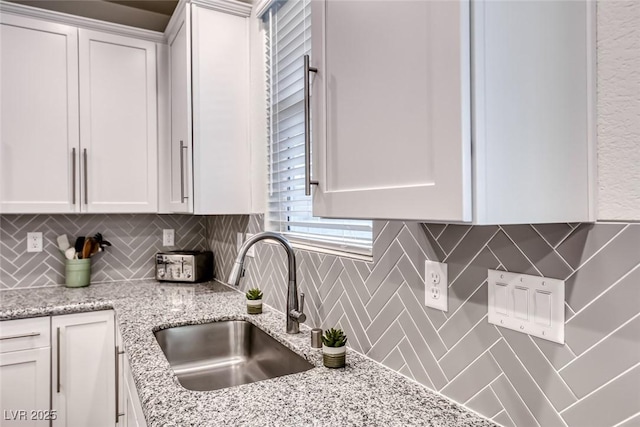 kitchen featuring a sink, light stone countertops, tasteful backsplash, and white cabinetry