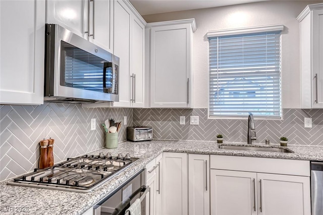 kitchen with light stone countertops, a sink, decorative backsplash, stainless steel appliances, and white cabinets