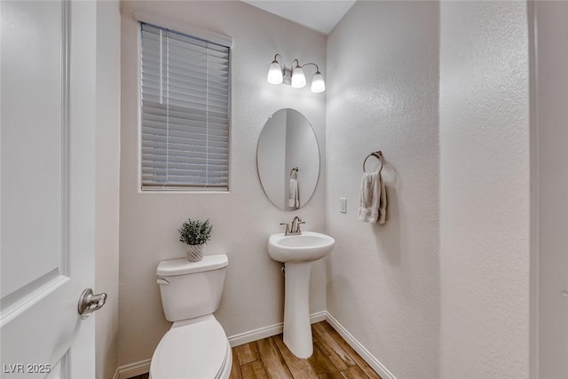 half bath with a sink, toilet, baseboards, and wood finished floors