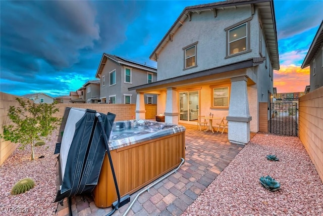 back of property at dusk featuring a gate, a fenced backyard, a hot tub, stucco siding, and a patio area