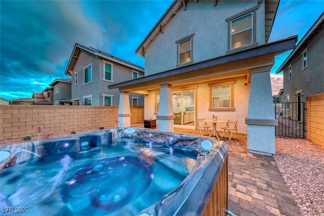 rear view of house featuring stucco siding, fence, and a hot tub