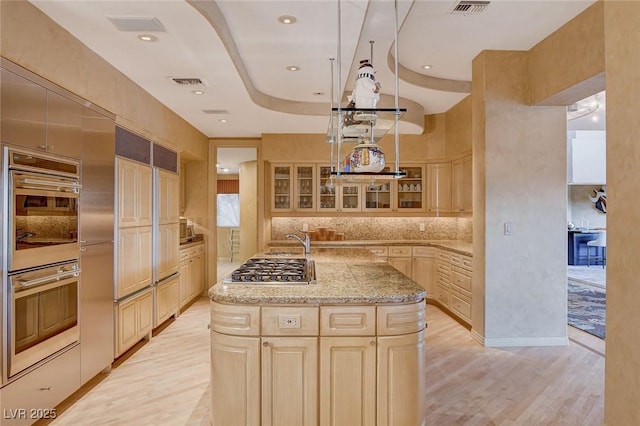 kitchen featuring light stone counters, visible vents, light wood-type flooring, and an island with sink