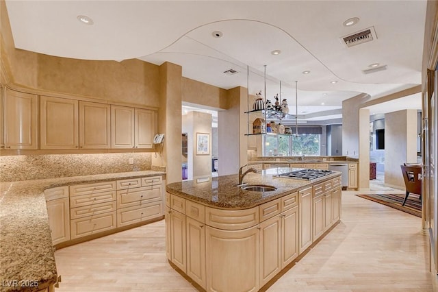 kitchen with visible vents, light stone counters, light wood-style flooring, stainless steel gas stovetop, and a sink