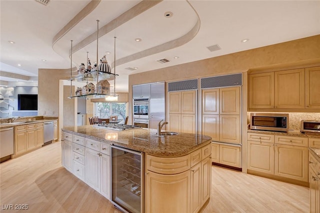 kitchen with visible vents, an island with sink, beverage cooler, a sink, and stainless steel appliances