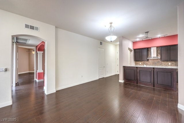 kitchen featuring visible vents, dark wood-type flooring, arched walkways, wall chimney exhaust hood, and decorative backsplash