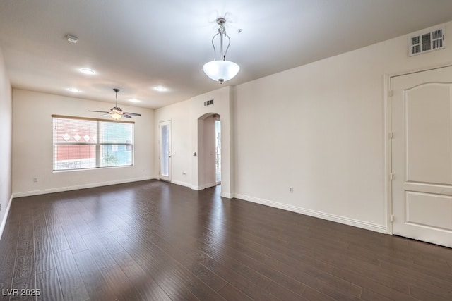 unfurnished living room with ceiling fan, visible vents, arched walkways, and dark wood-style floors