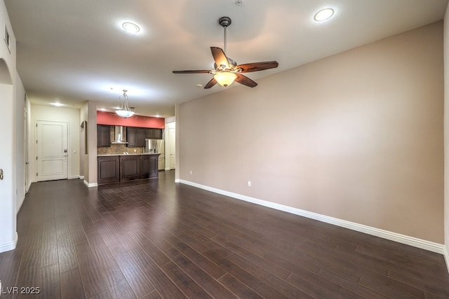 unfurnished living room with dark wood-type flooring, a ceiling fan, baseboards, and visible vents