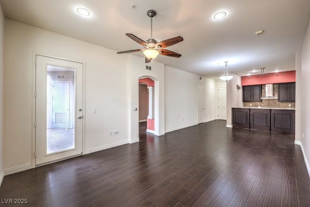 unfurnished living room with arched walkways, visible vents, a ceiling fan, and dark wood-style floors