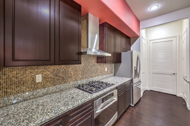 kitchen featuring tasteful backsplash, dark wood-type flooring, wall chimney range hood, light stone counters, and stainless steel appliances