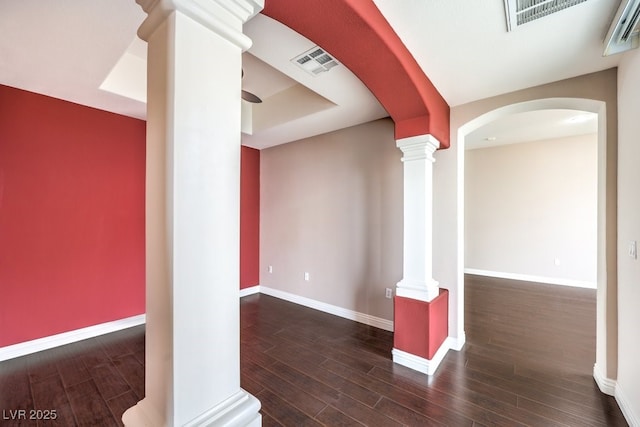 empty room featuring wood finished floors, visible vents, ornate columns, and baseboards