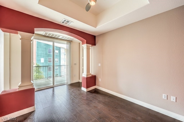 spare room featuring visible vents, dark wood-type flooring, baseboards, decorative columns, and a ceiling fan