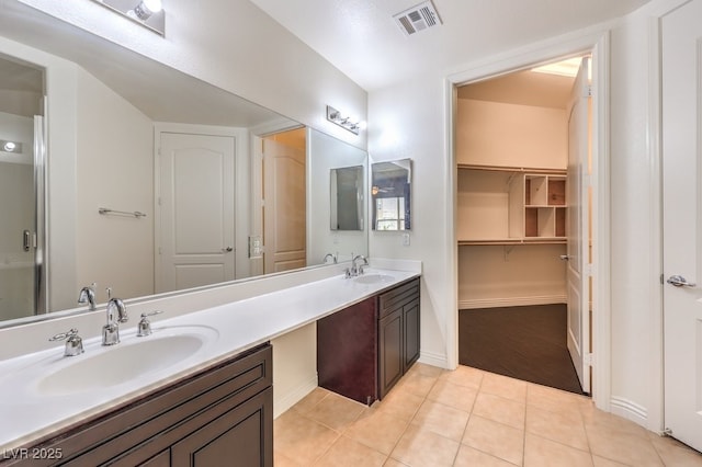 bathroom with visible vents, double vanity, a sink, tile patterned flooring, and a walk in closet