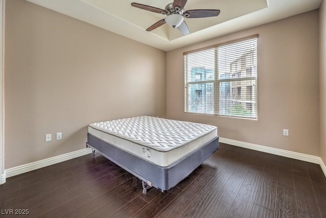 bedroom featuring baseboards, a raised ceiling, wood finished floors, and a ceiling fan