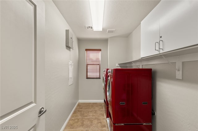 laundry room featuring a textured ceiling, cabinet space, separate washer and dryer, light tile patterned flooring, and baseboards