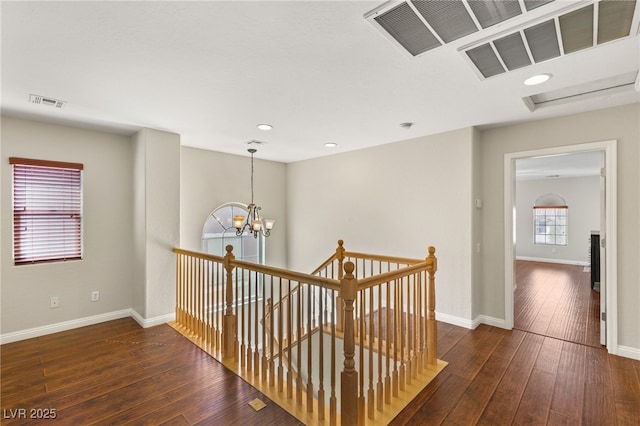 hallway with hardwood / wood-style floors, a notable chandelier, visible vents, and baseboards