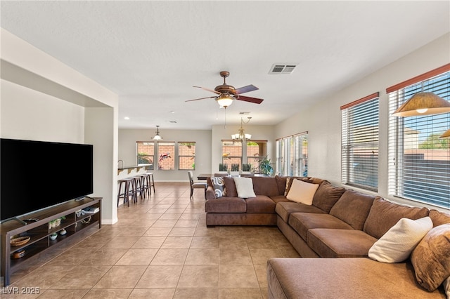 living room with light tile patterned floors, visible vents, ceiling fan with notable chandelier, and baseboards