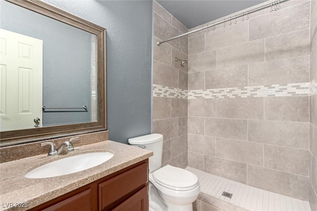 full bath featuring toilet, tiled shower, vanity, and a textured wall