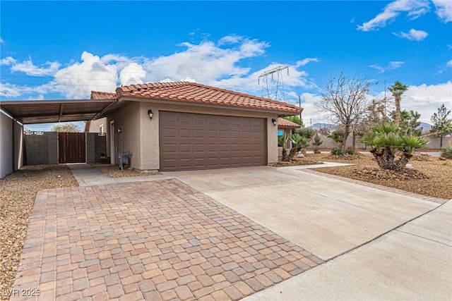 view of front of home with a tiled roof, stucco siding, a garage, driveway, and a gate