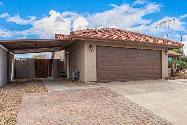 view of front of home with a tiled roof, concrete driveway, stucco siding, an attached garage, and a gate