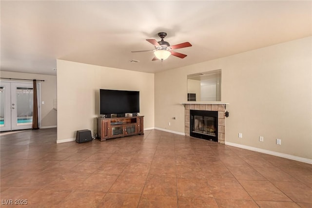 unfurnished living room featuring a tile fireplace, french doors, baseboards, and ceiling fan