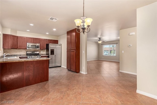 kitchen featuring baseboards, a sink, decorative backsplash, stainless steel appliances, and ceiling fan with notable chandelier