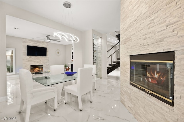 dining space featuring a stone fireplace, marble finish floor, stairway, and a ceiling fan