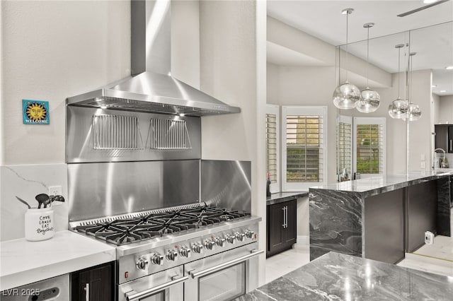 kitchen with stone countertops, pendant lighting, wall chimney range hood, range, and dark cabinets