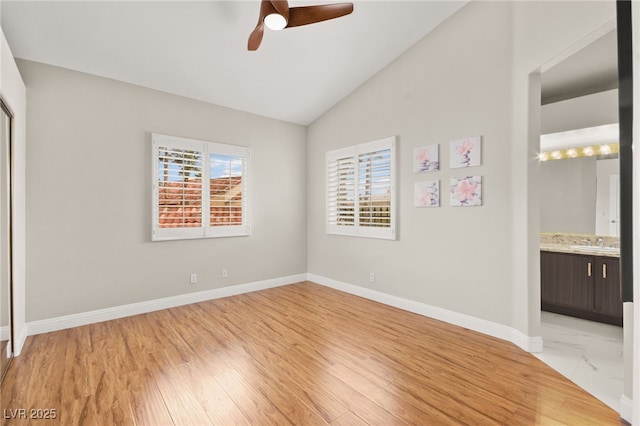 unfurnished bedroom featuring lofted ceiling, light wood-style floors, baseboards, and a sink